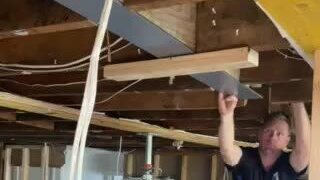 Interior of a partly opened-up room showing a steel beam fixed beneath timber framing, with props and services visible.