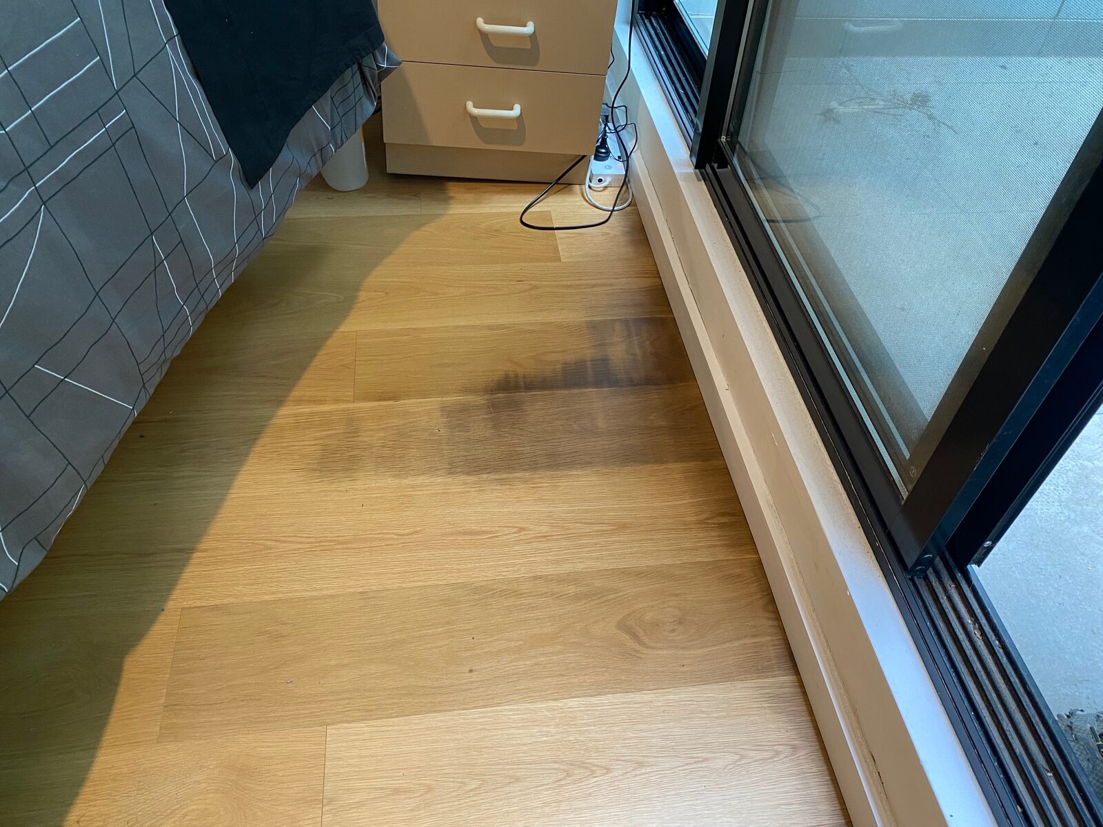 Timber floorboards beside a sliding door with a dark stain spreading across several boards.