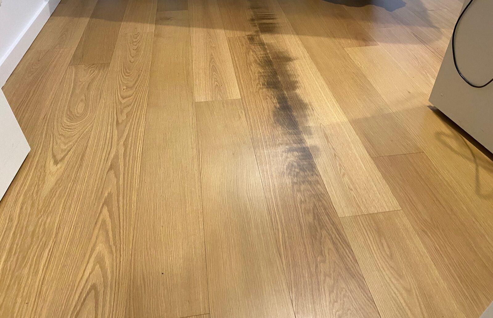 A wider view of timber flooring with a dark discoloured path running through the middle of several boards.